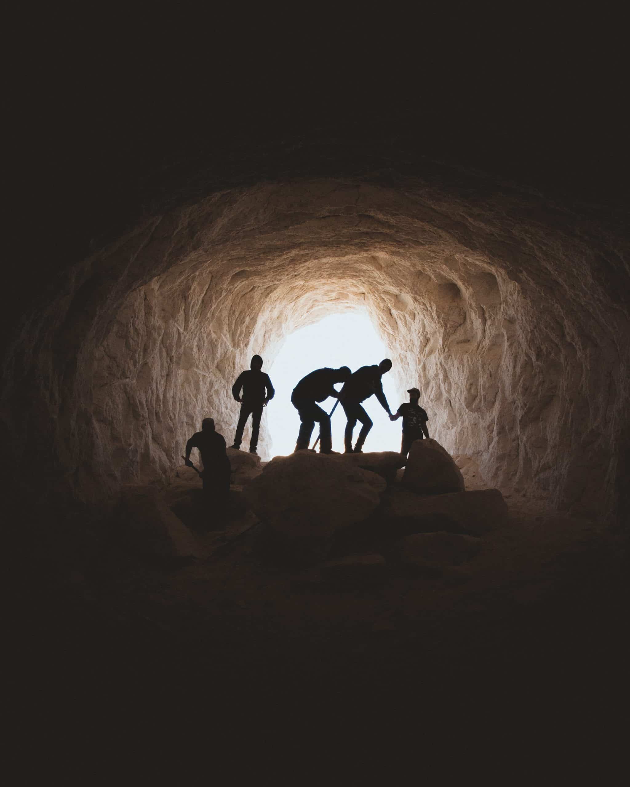 A group of cavers in silhouette with the light from the cave entrance