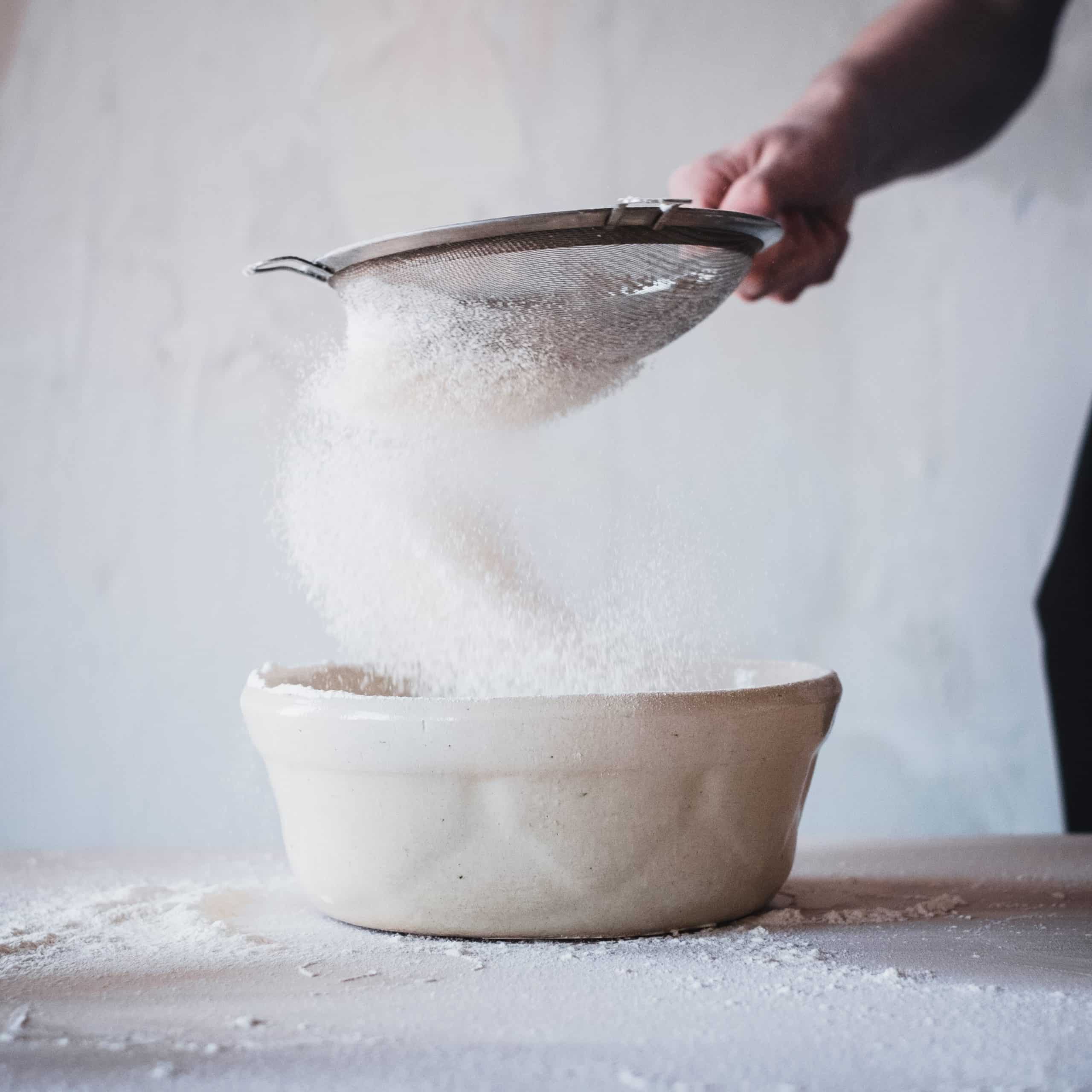 person sifting flour into a bowl